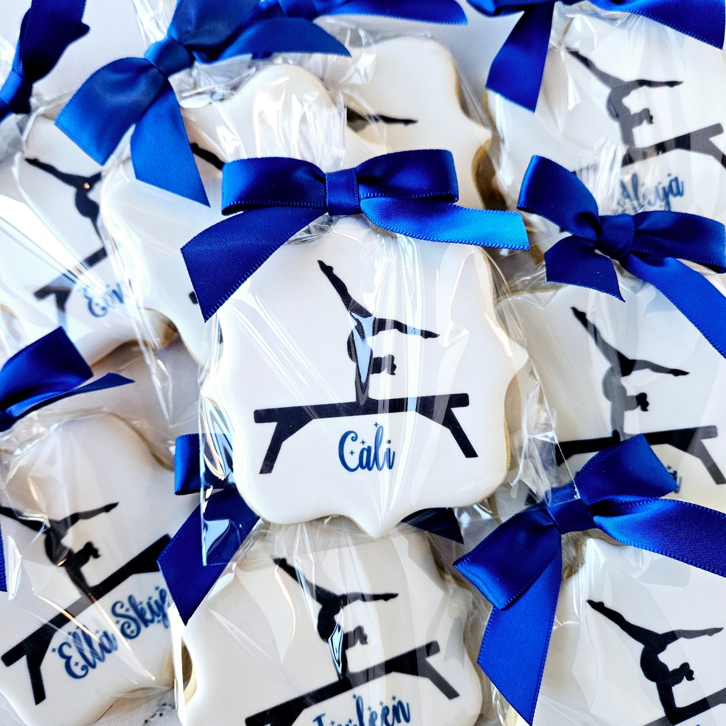 White cookies with blue ribbons and black silhouette designs on a white background. gymnastics cookies