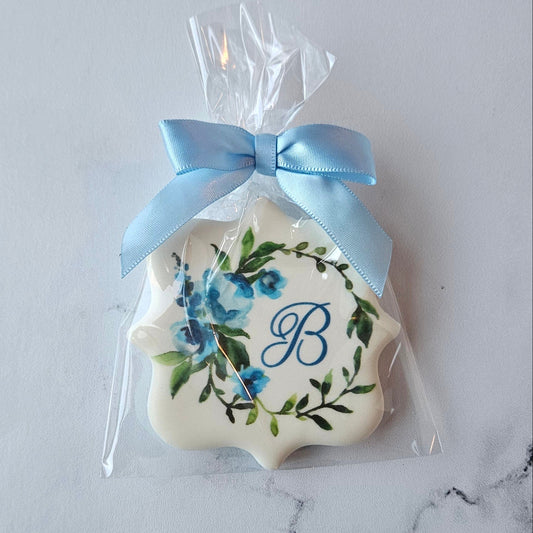 plaque shape logo cookie with blue monogram and floral wreath and light blue ribbon