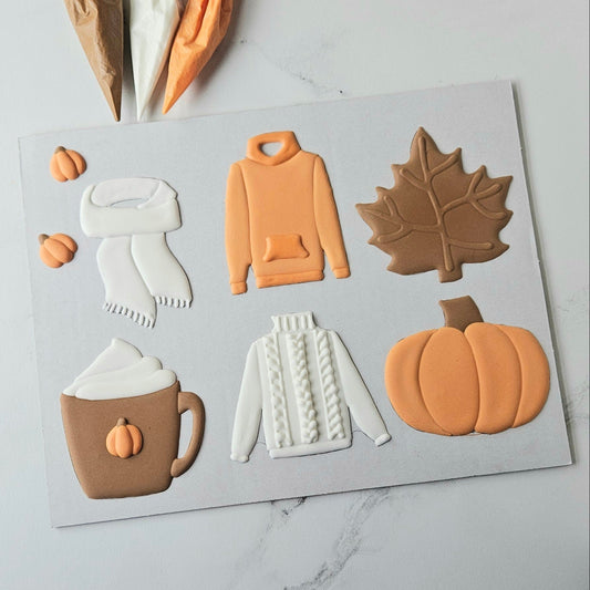 Decorative cookies shaped like a maple leaf, hoodie, mug with hot chocolate, and pumpkin on a white background. Cookie decorating class in Loganville, Georgia